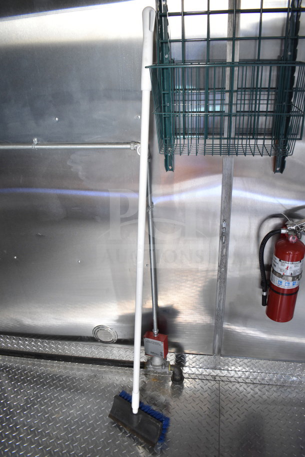 Interior view of the 2021 Cruising Kitchens food trailer showing a fire extinguisher, wall-mounted basket, and cleaning tools.