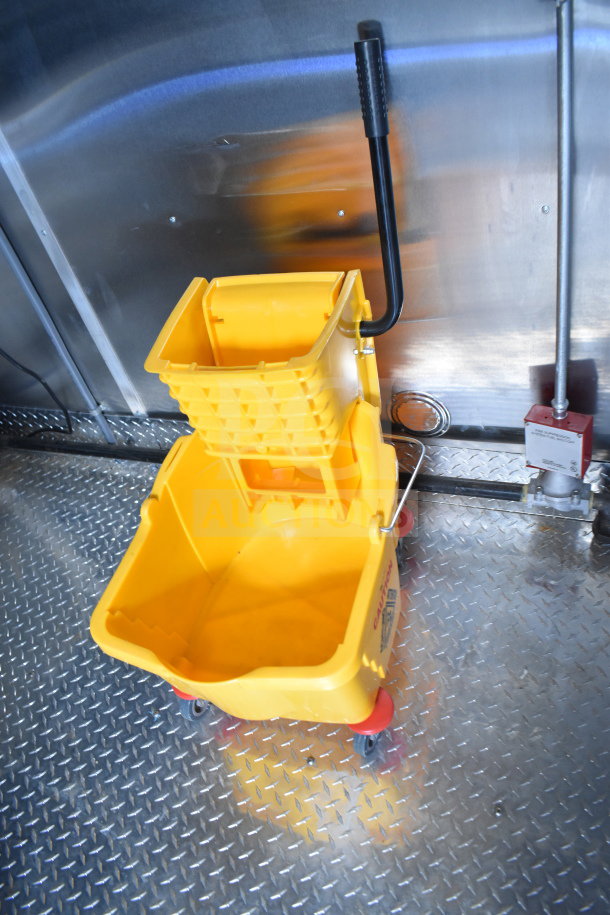 Yellow mop bucket with wringer and black handle on metal diamond plate floor.