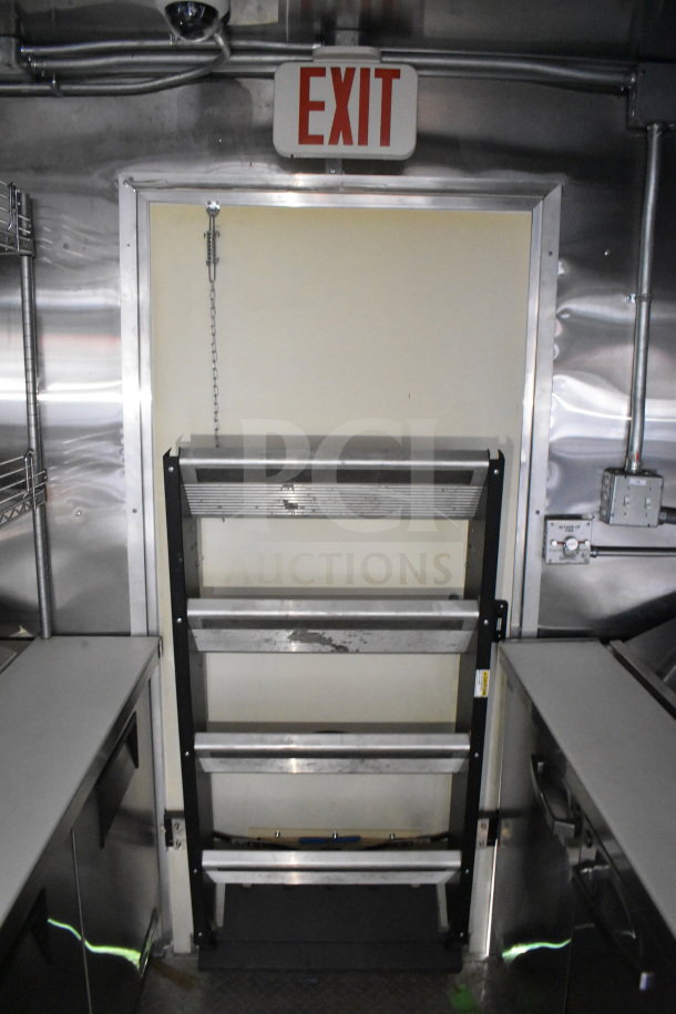 2021 Cruising Kitchens food trailer interior with metal shelving, clean surfaces, and an exit sign overhead.