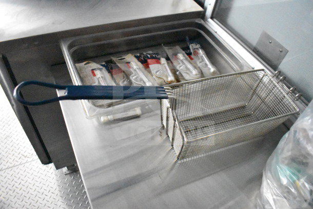 Stainless steel food tray with wire basket and blue-handled utensil inside a 2021 Cruising Kitchens food trailer.