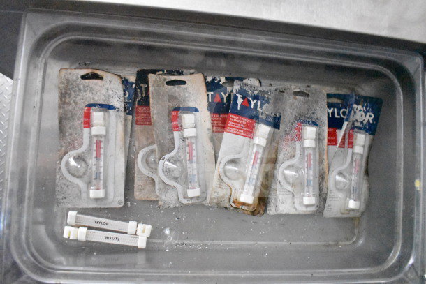 Thermometers in packaging labeled Taylor Brand, some with visible wear, in a metal storage setting.