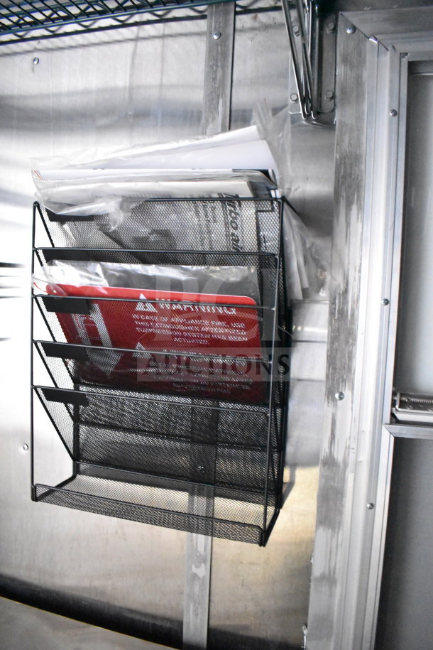 Metal document holder with safety warning signs inside a Cruising Kitchens food trailer.