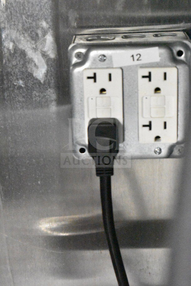 Electrical outlet in 2021 Cruising Kitchens food trailer. Outlet has dual plugs, black cord, and label marked "12".
