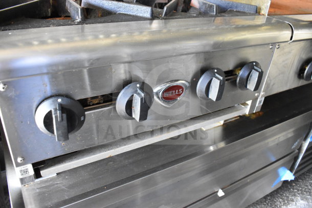 Stainless steel Wells gas range with four control knobs, part of 2020 Diamond Cargo 8.5'x24' food trailer. Slight wear visible.