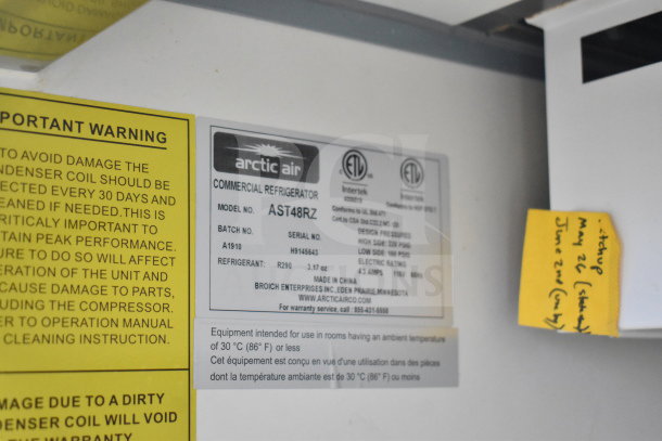 Yellow warning label and Arctic Air commercial refrigerator tag on interior wall, model AST48RZ, serial H9145643.