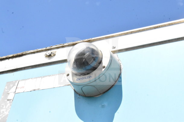 Security camera on the exterior of a blue food trailer, branded Avigilon.