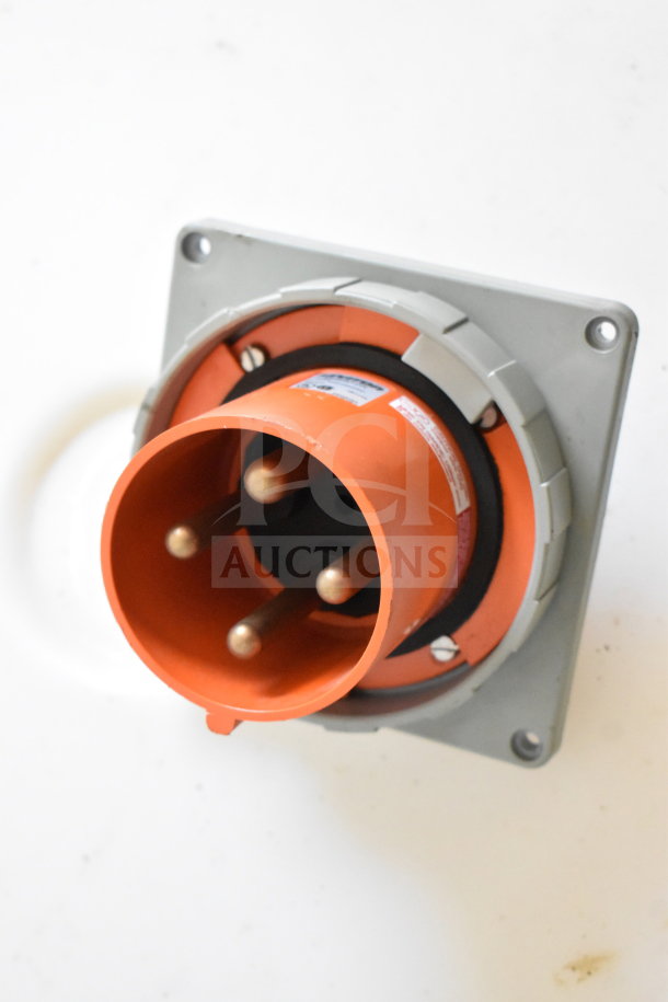 Orange industrial power connector, three-pronged, mounted on a metallic base, used for electrical connections.