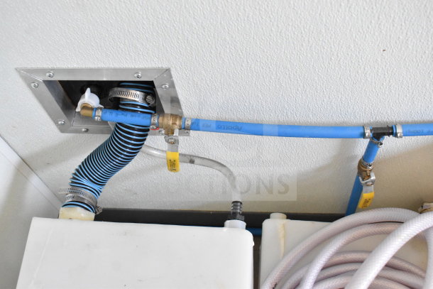 Close-up of plumbing and hose connections inside a 2021 Diamond Cargo 8.5'x24' food trailer. Includes blue and white hoses.