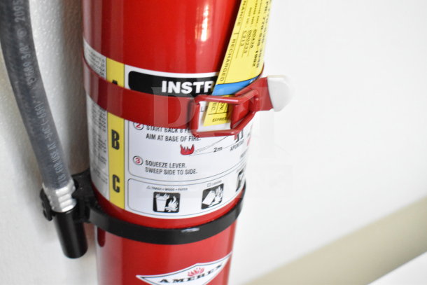 Image of a fire extinguisher with visible instructions and labels attached, mounted on a wall.