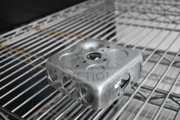 A metal electrical box with multiple circular knockouts resting on a wire shelf.