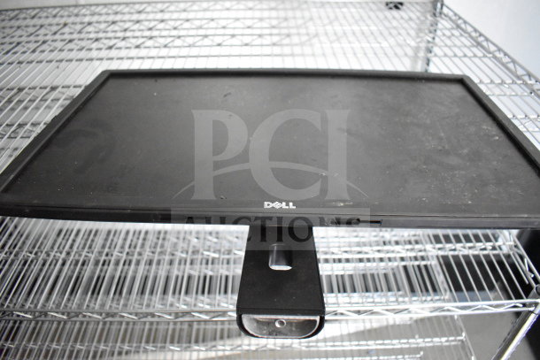 A Dell monitor on a wire shelf, featuring a black bezel and stand, with slight dust visible on the screen.