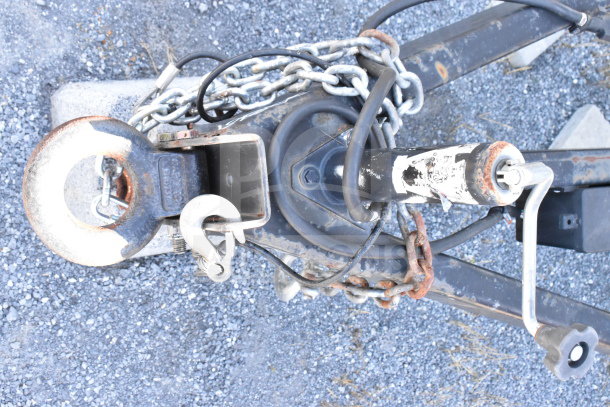 2021 Diamond Cargo trailer hitch with visible chains and a crank handle on gravel surface, showing mild rust and wear.