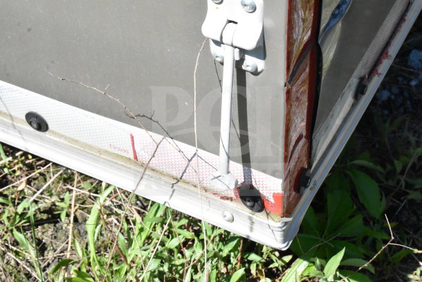 2021 Diamond Cargo 8.5'x24' trailer corner with reflective tape, hinge, and vegetation nearby.