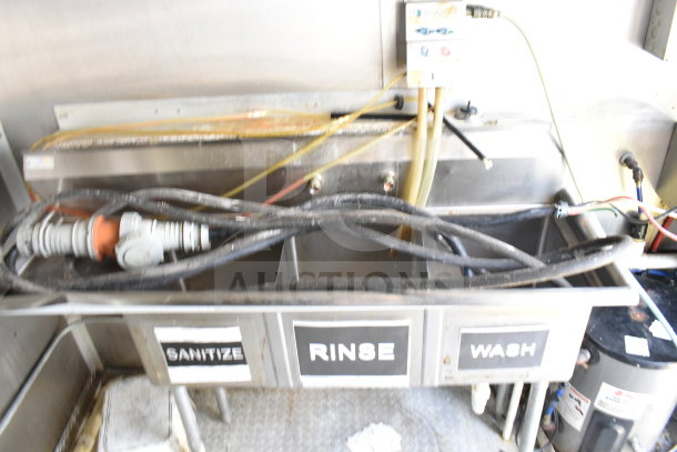 2019 Diamond Cargo 8.5'x24' food trailer kitchen area with triple sink labeled sanitize, rinse, wash, and visible pipes.