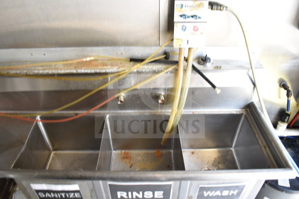 Three-compartment sink in Diamond Cargo food trailer, labeled 'Sanitize,' 'Rinse,' 'Wash.' Visible hoses and connections.