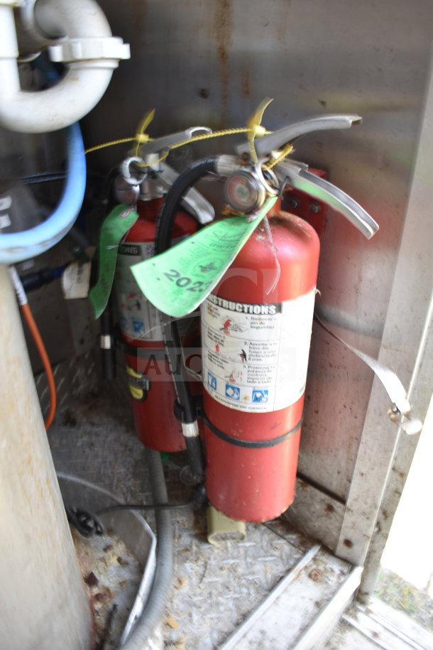 2019 Diamond Cargo food trailer's fire safety system with two red extinguishers, labels dated 2023 visible.