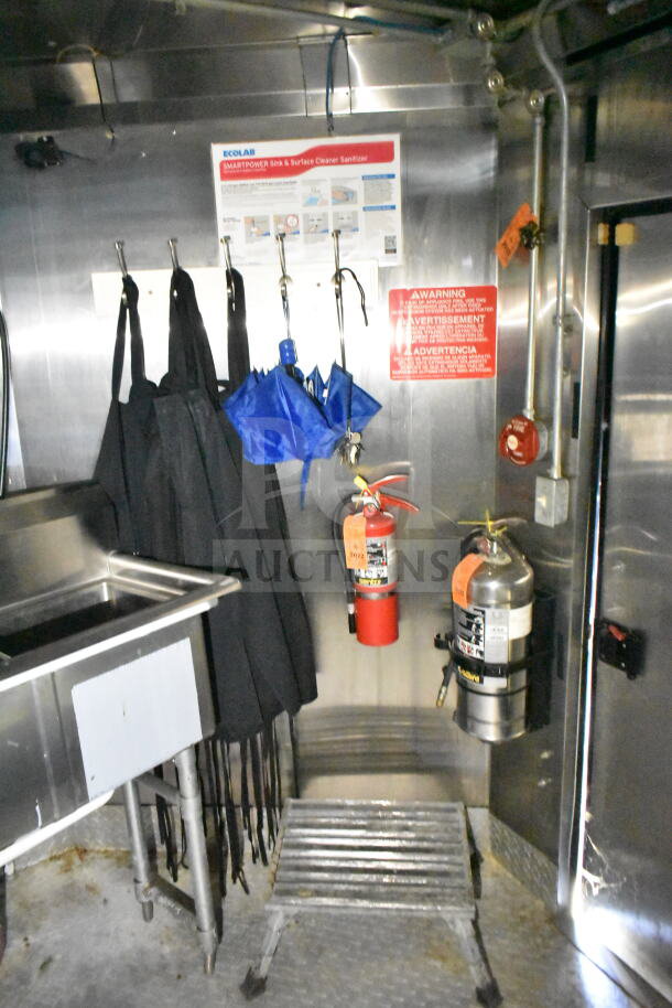 Interior of 2020 LGS TX food trailer with stainless steel sink, aprons, fire extinguishers, warning sign, and step stool.