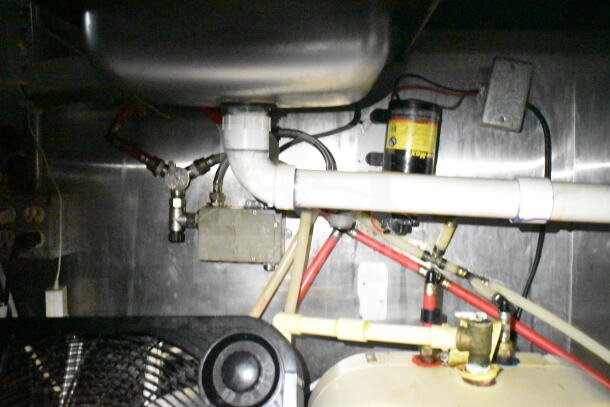 Interior view of 2020 LGS TX food trailer, showing piping and mechanical components. Visible wiring and connectors in stainless steel setting.