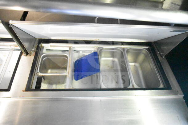 Stainless steel food trailer refrigeration compartment with multiple food trays, one with a blue lid.