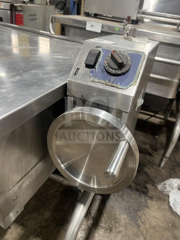 Commercial stainless steel braising pan with tilting feature, control panel, visible wear, mounted on sturdy legs.
