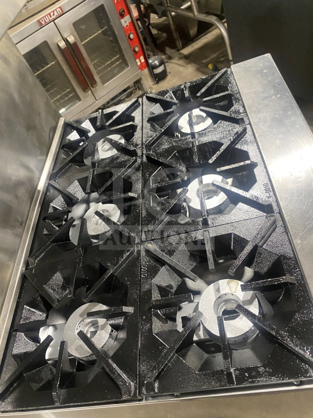 CookRite stainless steel 6-burner range/oven combo with backsplash, overhead salamander shelf, and wired oven rack on casters.