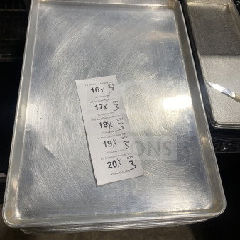 Commercial stainless steel baking sheet pan, gently used, showing minor wear. Includes auction label with bidding details.