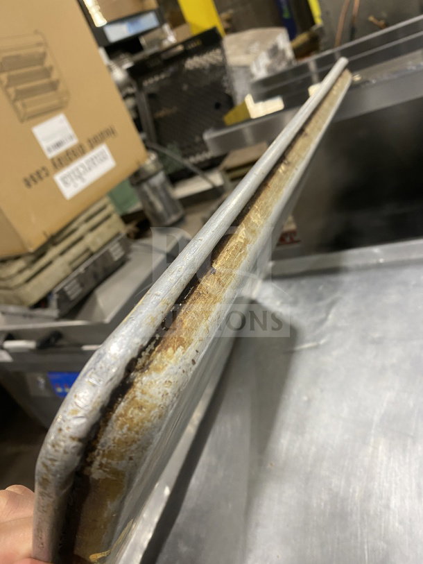 Commercial-grade stainless steel baking sheet pan, used, showing edge wear and discoloration. Ideal for large-scale baking.