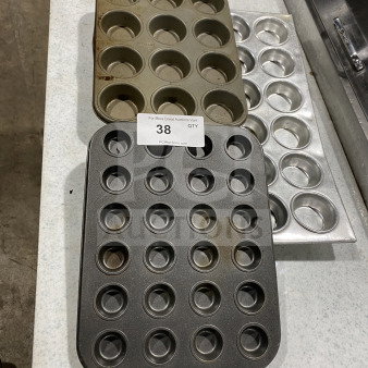 Three commercial stainless steel multi-cup muffin and cupcake pans, varying styles, slightly used. Auction tag visible.