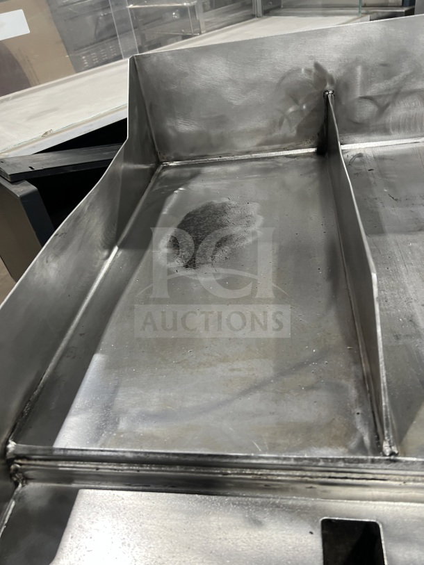 Commercial stainless steel flat-top griddle with two sections, back and side splash, on casters, showing wear.