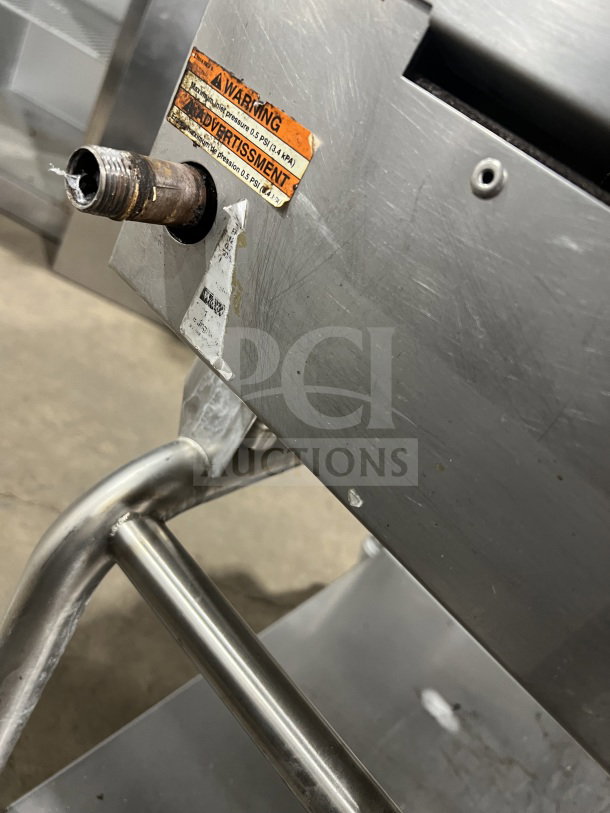 Commercial stainless steel flat-top griddle with heavy-duty build, dual sections, back and side splash, casters; visible warning label.