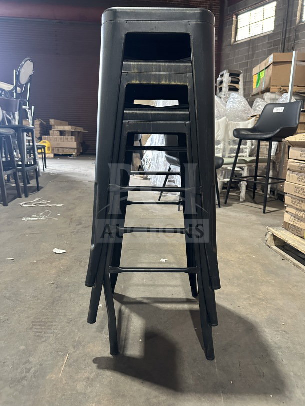 Brand new Astor matte black backless metal counter-bar stools, industrial Tolix-style, stacked in a warehouse setting.