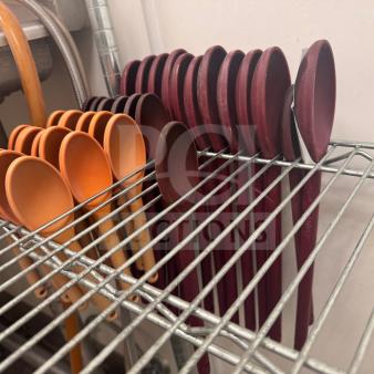 Heat-resistant plastic cooking spoons in orange and red hues, neatly arranged on metal shelving, varied sizes, new condition.