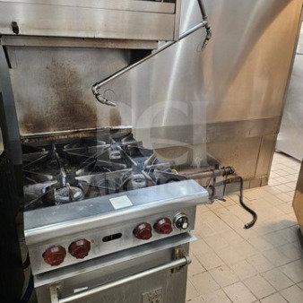 Wolf commercial 6-burner gas range with red knobs, featuring a mounted salamander broiler above, in working condition.