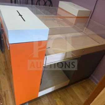 Modern retail display checkout counter with orange and white panels, clear acrylic top, and drawer. Slight wear visible.