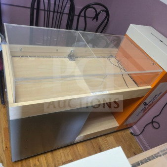 Retail display/checkout counter with glass top, wood finish, storage shelves. Features an orange and gray section, minor wear.