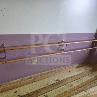 Wall-mounted wooden ballet barre system with dual bars, metal brackets, and light wood finish on a purple wall. Good condition.