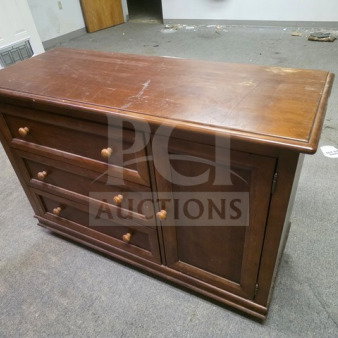 Vintage wooden dresser with three drawers and a door, showing visible wear. Dark finish and wooden knobs.
