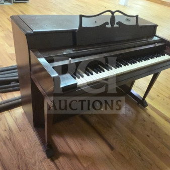 Wurlitzer spinet piano in dark wood finish, showing some wear. Keyboard and pedals visible.