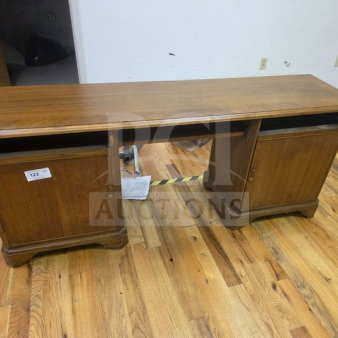 Wood kneehole desk with dual cabinets, light brown finish. Visible label reads "125." Minor wear on surfaces, sturdy condition.