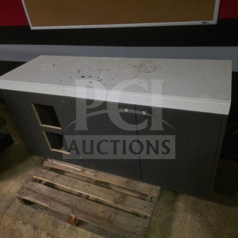 Gray trade show counter, dual cabinets, white top with stains, moderate wear, resting on a wooden pallet.