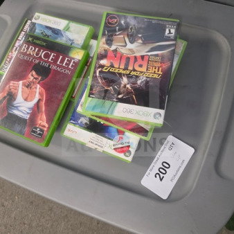 Lot of miscellaneous video games and movies on a plastic table. Includes Xbox titles like "Bruce Lee: Quest of the Dragon." Auction tag shows number 200.