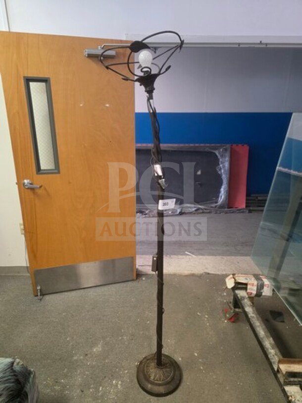 Tall vintage floor lamp with intricate wrought iron design, single bulb holder. Base shows signs of wear, no visible shade.