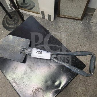 Vintage entrenching tool with a collapsible metal handle, serrated edge, and label marked "220 PCUauctions.com." Signs of wear visible.