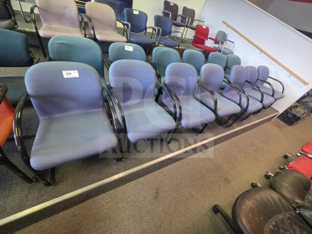 Lot of 7 office chairs with blue fabric upholstery, black armrests, and metal frames. Used condition, visible numbering tags.