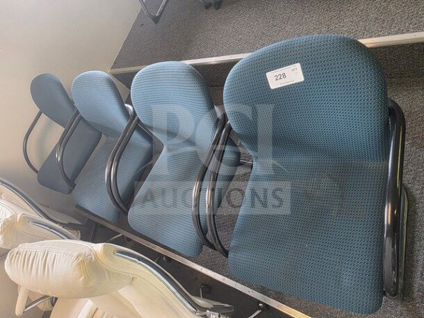 Lot of 4 office chairs with blue fabric upholstery, black metal armrests, and legs. Visible label with number 228. Some wear shown.