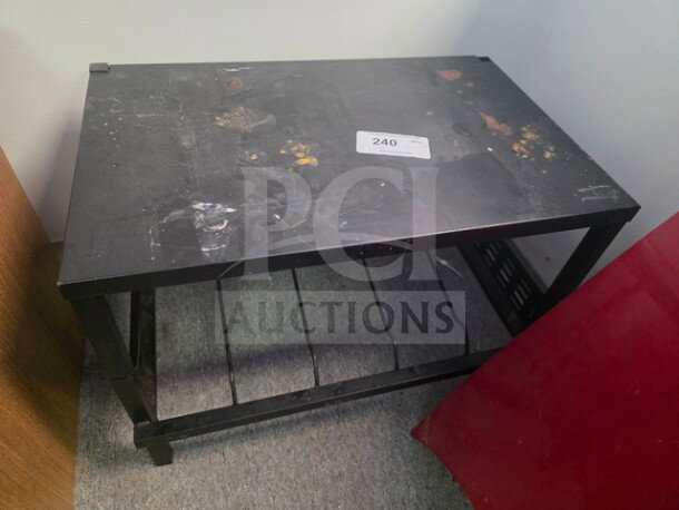 Black work table with metal frame and two-tier shelving, showing signs of wear and surface stains. Label with number "240" attached on top.