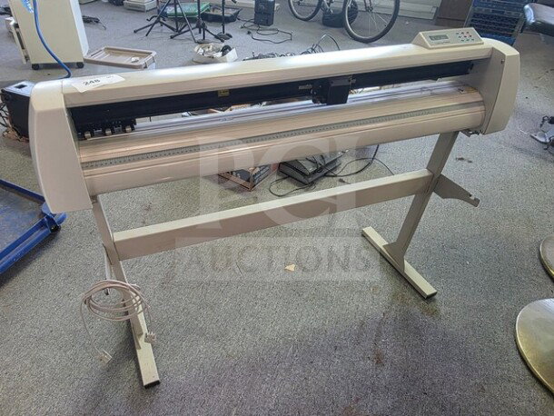 Cutting plotter on stand, white, in used condition. Features a control panel and cutter head. Power cable included.