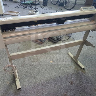 Cutting plotter on stand, white, in used condition. Features a control panel and cutter head. Power cable included.