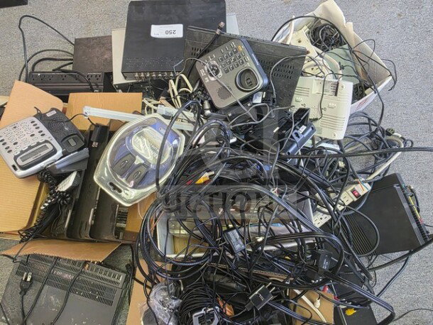 Lot of miscellaneous electronics including phones, cords, power strips, and routers in used condition. Tags show numbering and sorting indications.