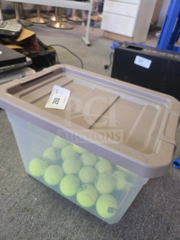 Lot of tennis balls in a clear plastic storage bin with taupe lid. Bin labeled with auction tag "220". Balls appear gently used.